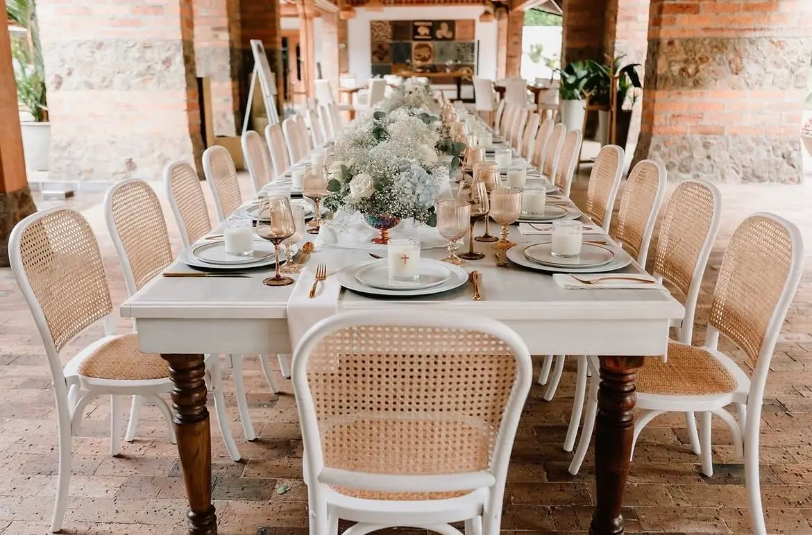 Mesa larga con sillas blancas de mimbre y centro de flores