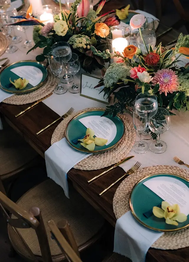 Mesa puesta con platos verdes, servilletas blancas y flores